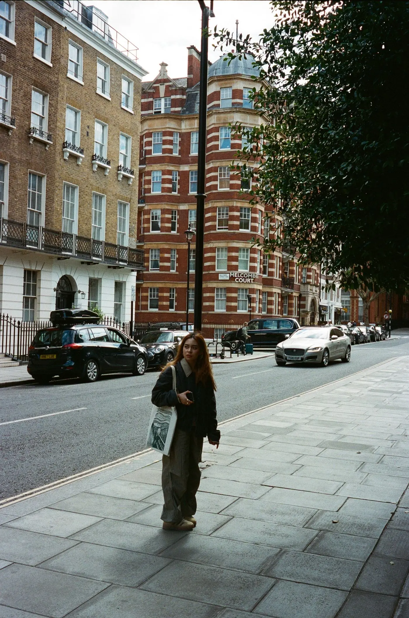 A woman walking along a London street of red-brick mansion blocks