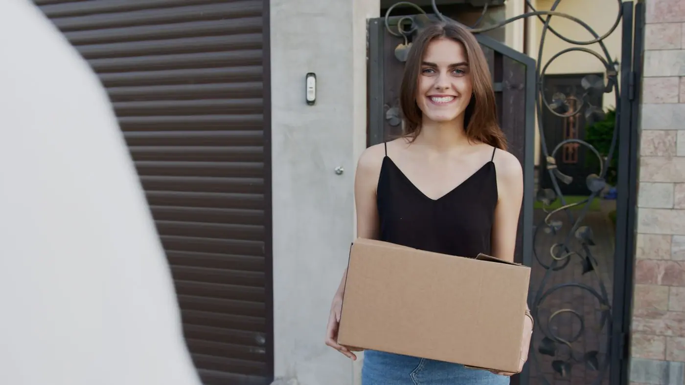 A smiling woman holding her delivery at her front gate
