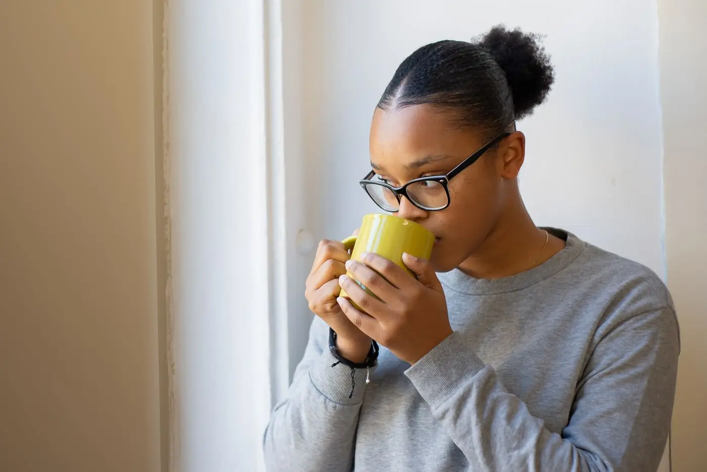 A woman enjoying a warm drink by the window at home